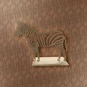 Metallic zebra sculpture on a marble base against a patterned wall.